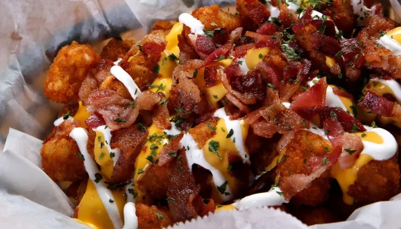 Crispy tater tots with cheese sauce, crumbled bacon, and green herbs.