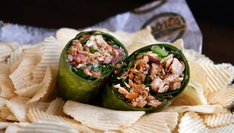 Sliced green wrap with chicken and vegetables, served on potato chips.