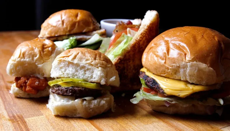 Cheeseburger, sliders, and a triangular sandwich on a wooden surface.
