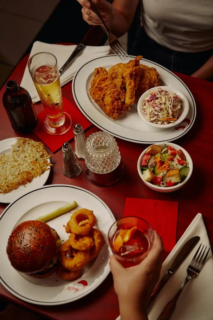 Overhead view of two people eating fried chicken, a burger, and drinks.