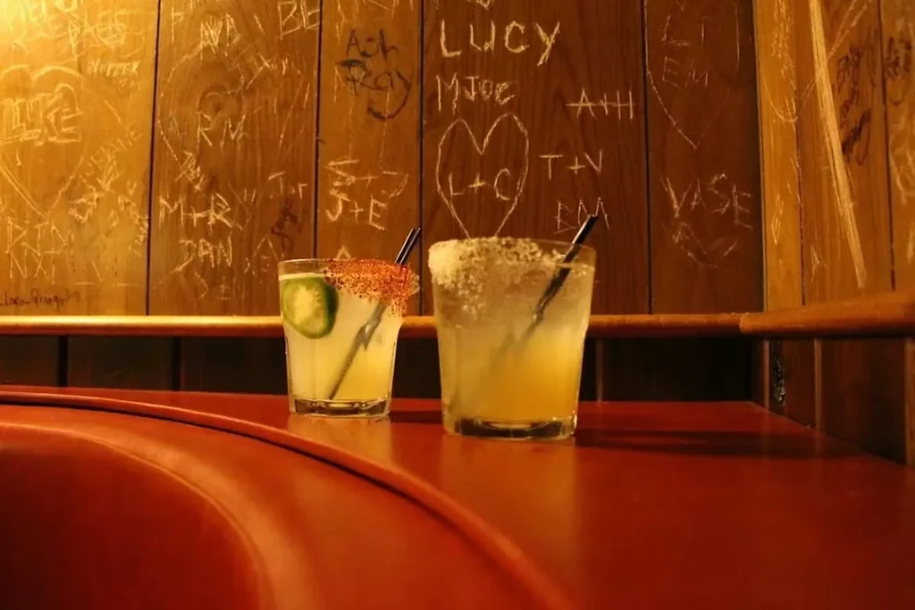 Two margaritas with chili and salt rims against a carved wooden wall.