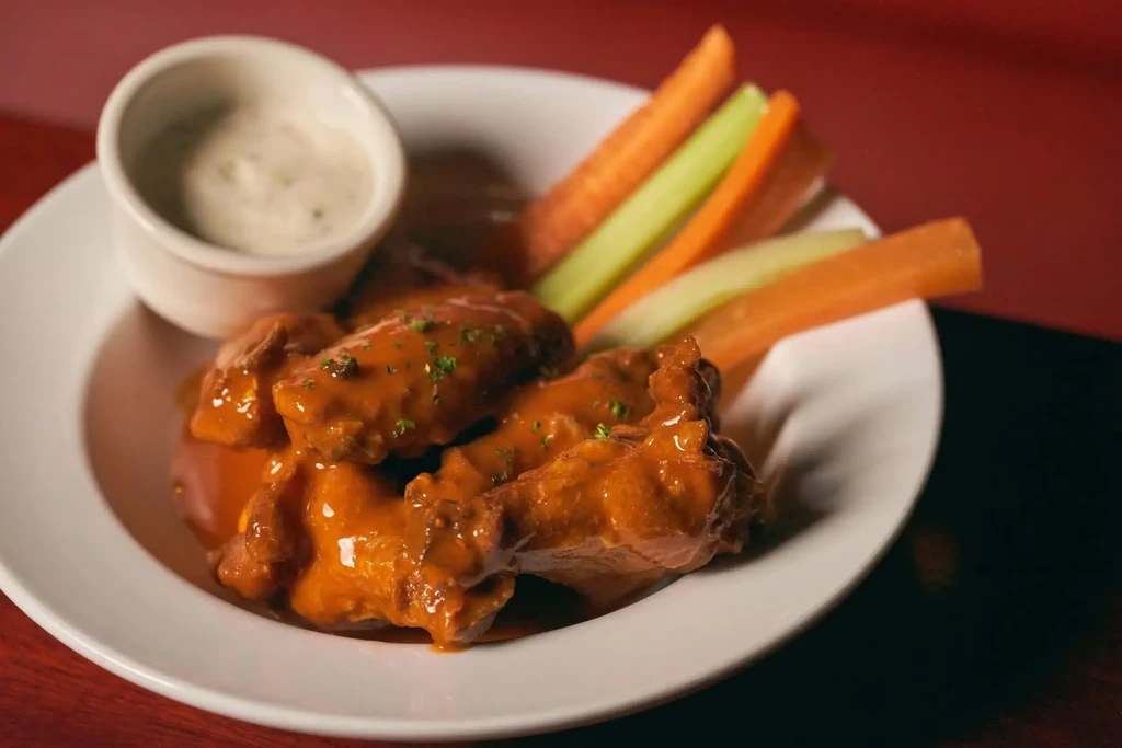 Plate of saucy buffalo wings, creamy dip, carrots, and celery.