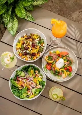 High-angle shot of three colorful salads and three drinks on a table.