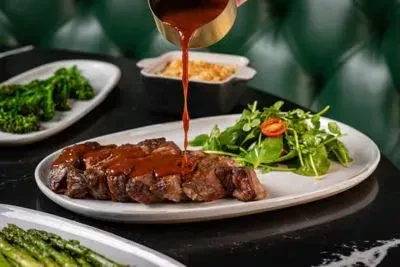 Sauce being poured over sliced steak, salad, and restaurant sides.