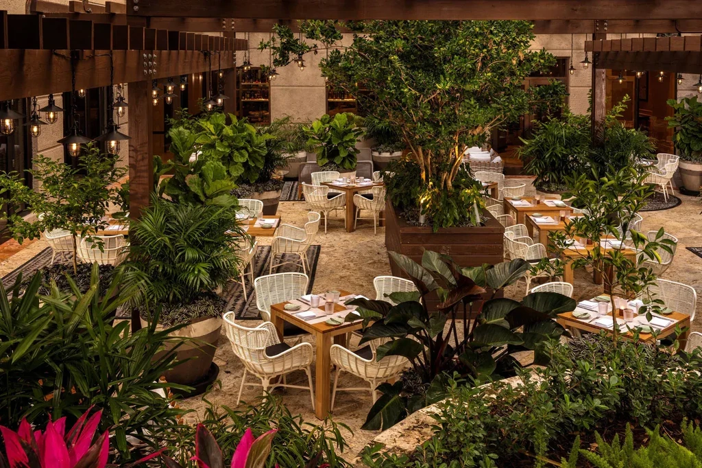 Empty outdoor restaurant patio with dining sets, lush plants, and lit pergola.