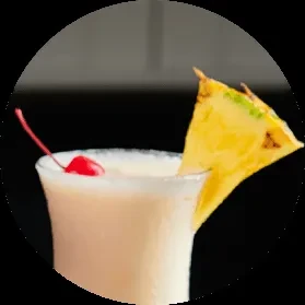 Close-up of a creamy blended cocktail with a cherry and pineapple.