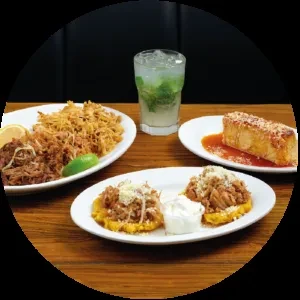 Plates of shredded meat, plantain dishes, fried cheese, and a mojito.