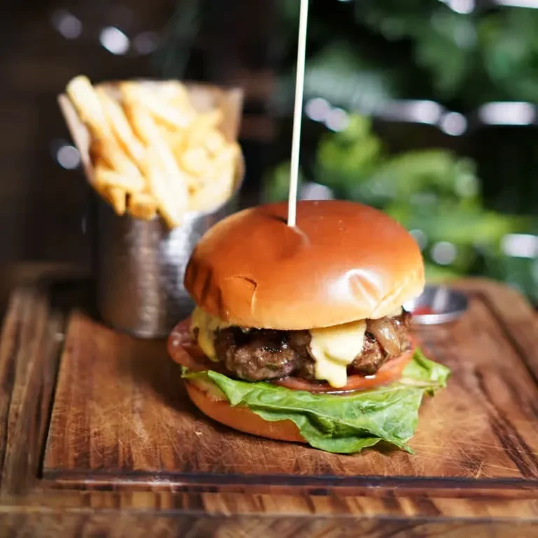 Gourmet burger with fries and dipping sauce on a wooden board.