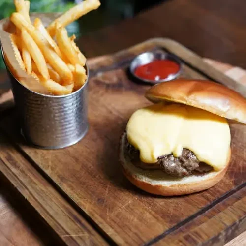 Open-faced burger with melted cheese, fries, and ketchup on a wooden board.