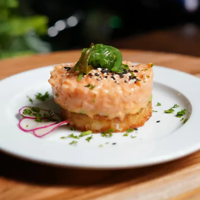 Cylindrical salmon tartare, garnished with seaweed, herbs, and radish.