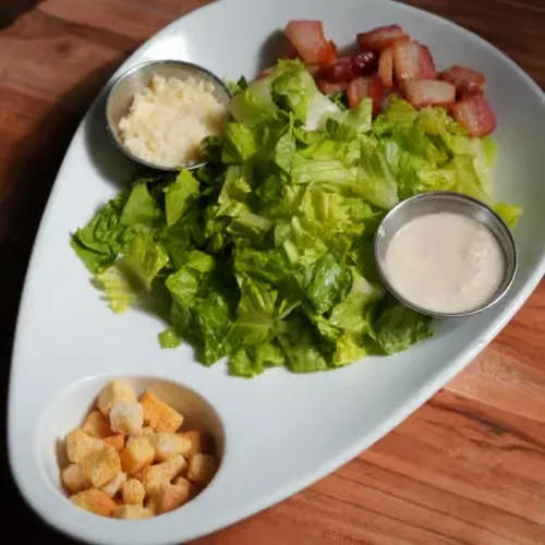 Deconstructed salad with lettuce, Parmesan, bacon, croutons, and dressing.