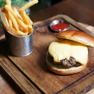 Top-down cheeseburger, fries in cup, ketchup on rustic wooden board.