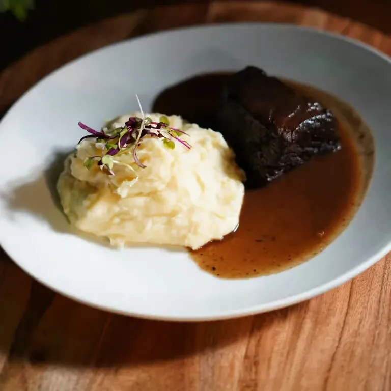 Braised short rib, mashed potatoes, gravy, and microgreens on a plate.