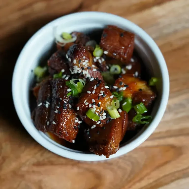 Small white bowl of glazed pieces with sesame and scallions.