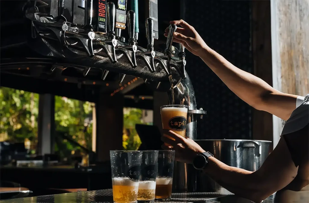 Bartender's hands pour golden beer from a tap into a 'tap42' glass.
