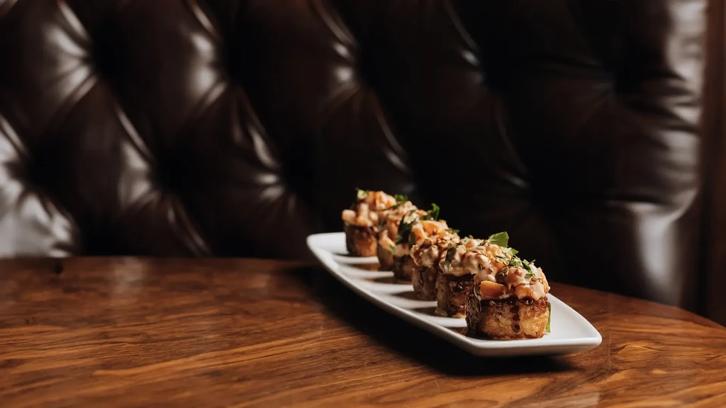 Dish with five golden portions topped with creamy tartare, herbs, and sauce.