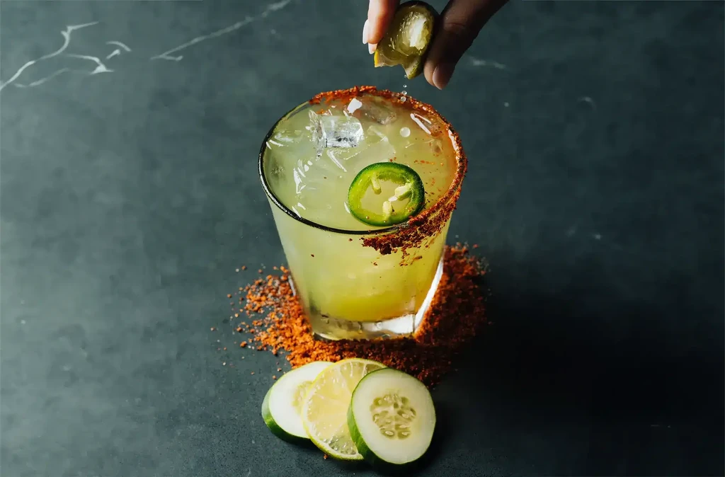 Hand squeezing lime into a chili-rimmed citrus cocktail with jalapeño.