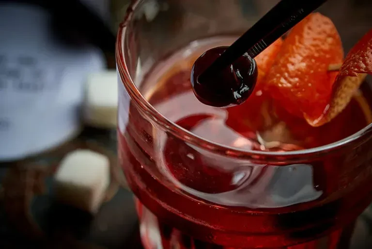 Vibrant red cocktail with cherry and twisted orange peel, close-up.