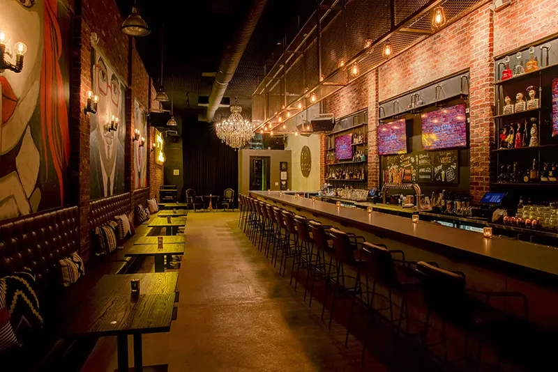 Dimly lit bar interior: leather booths, abstract art, stocked bar, chandelier.