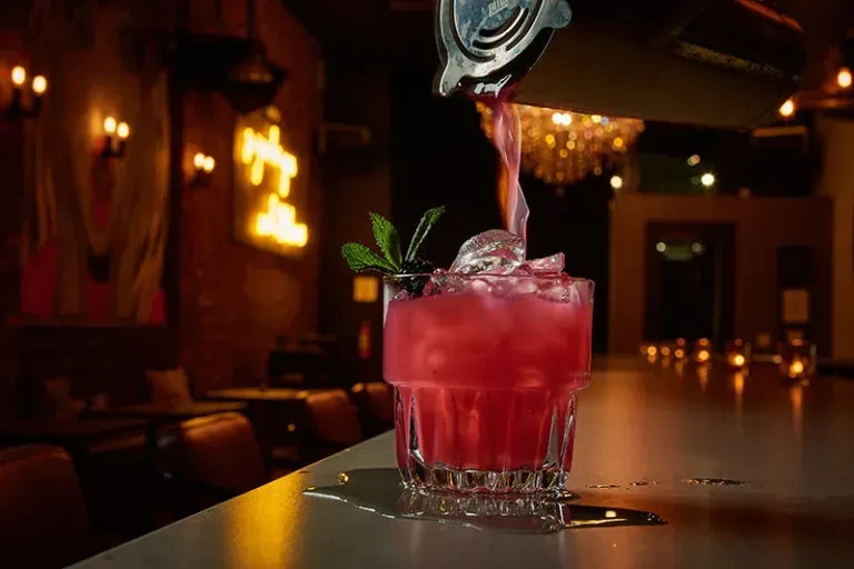 Red cocktail poured from shaker into glass with ice and mint.