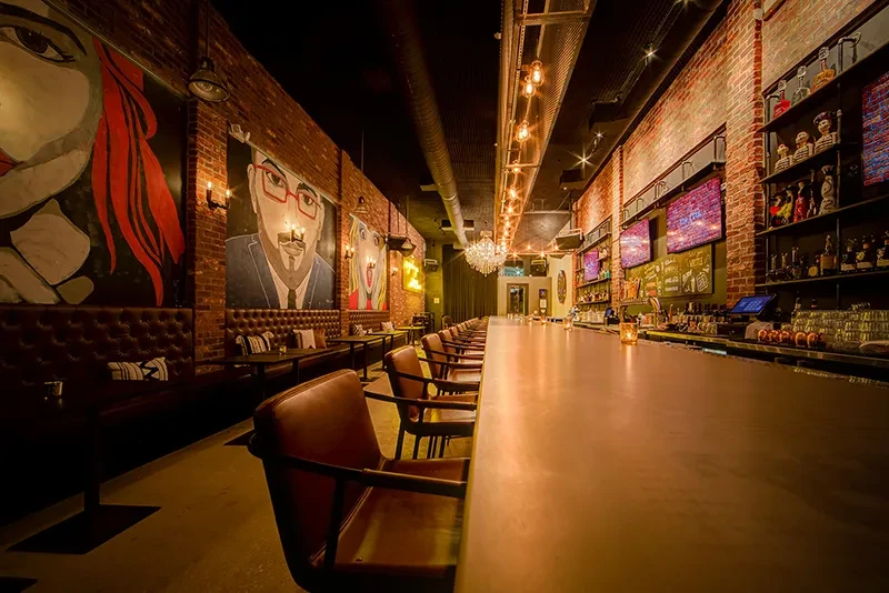 Stylish bar interior: brick walls, pop-art murals, and a long counter.