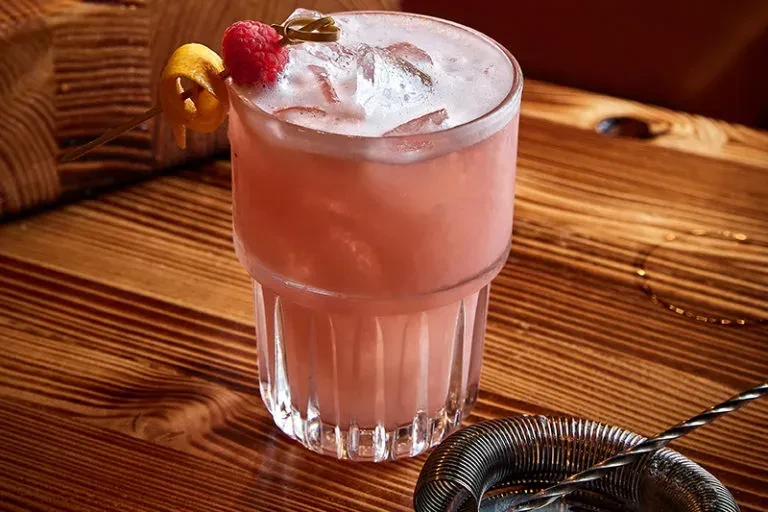 Frothy pink cocktail with ice, raspberry, citrus on wooden bar.