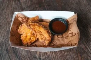 Crispy golden-brown fried chicken tenders in a tray with dipping sauce.