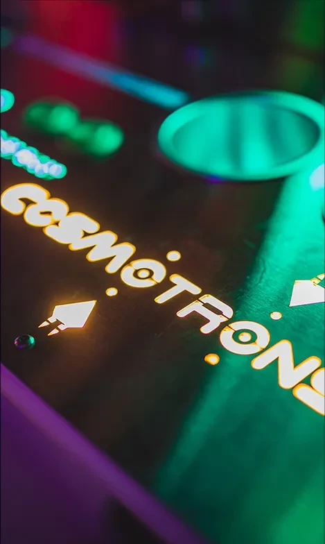 Glowing 'cosmotron' text and pixelated spaceship in an arcade setting.