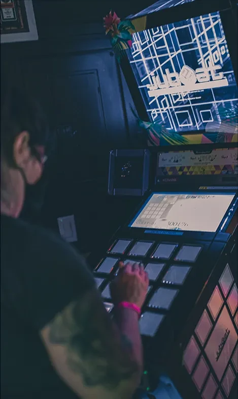 Person with mask and arm tattoos plays Jubeat arcade game.