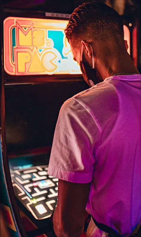 Person plays Ms. Pac-Man arcade game, lit by machine's glow.