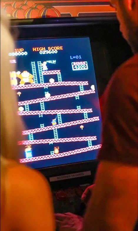 Two people playing a classic Donkey Kong arcade game screen.