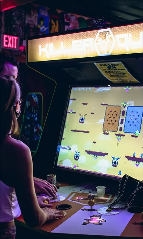 Low-light scene of two people playing Killer Queen arcade game.
