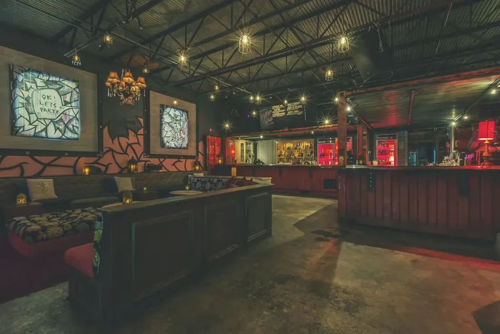 Stylish bar interior, corrugated ceiling, plush booths, glowing red bar.