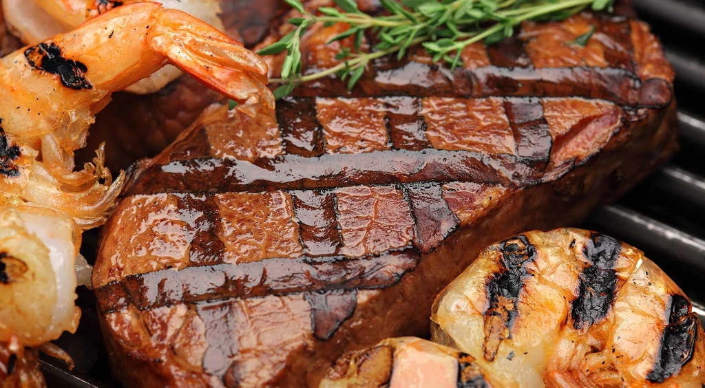 Close-up of grilled steak, shrimp, and vegetables with grill marks.