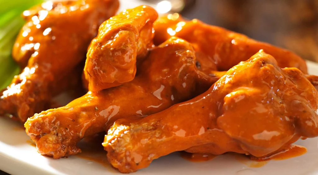 Glossy orange sauced chicken wings on a white plate.