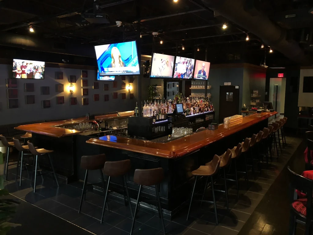Dim, empty U-shaped bar with stocked back bar and TVs.