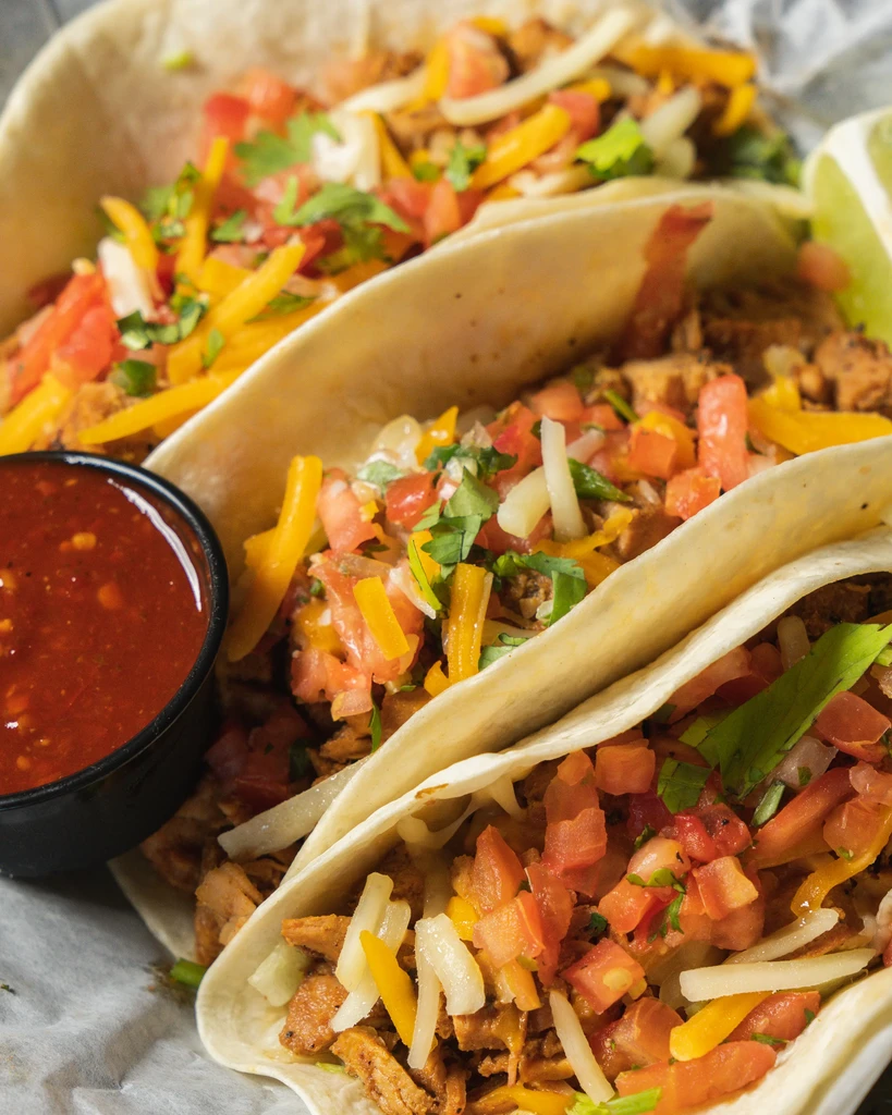 Three soft-shell tacos with meat, pico, cheese, salsa, and lime.