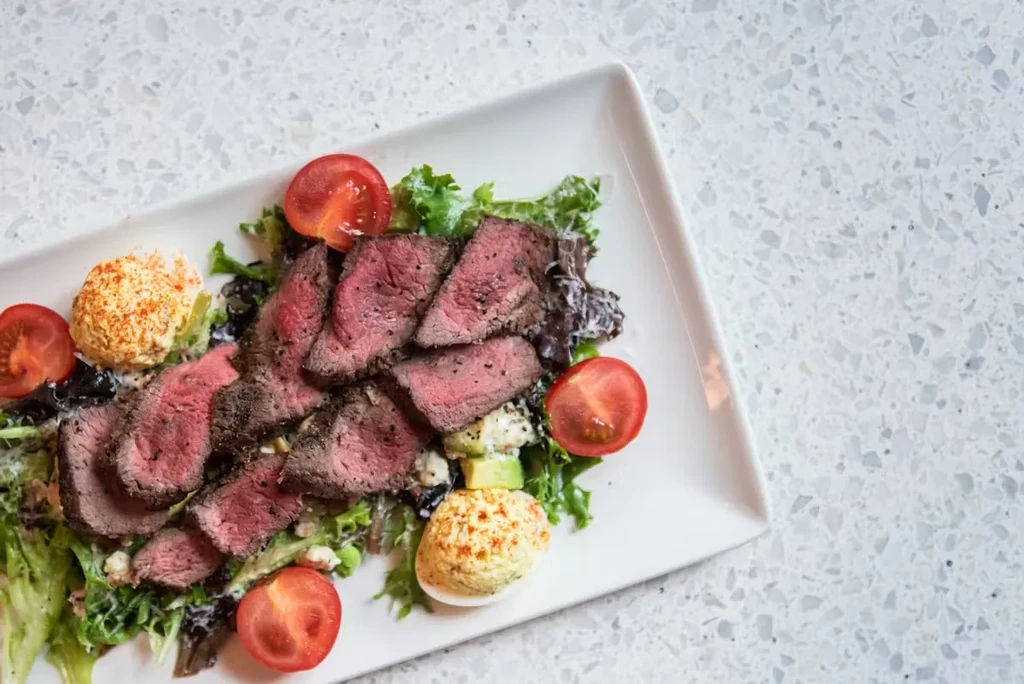 Medium-rare steak salad with deviled eggs, mixed greens, and tomatoes.