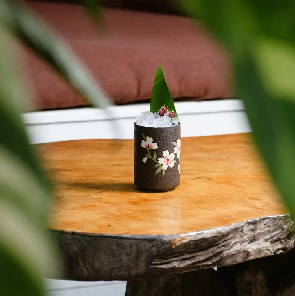 Cocktail in cherry blossom mug with garnish on rustic wooden table.