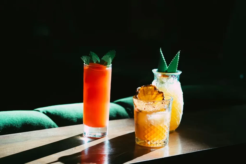 Three garnished drinks, including a pineapple glass, on dark wood.