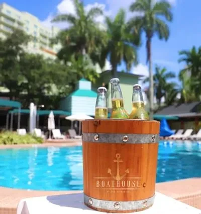 Ice bucket with 'BOATHOUSE' bottles by a sunny resort pool.