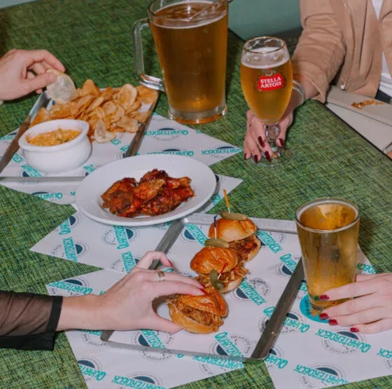 Table with wings, sliders, chips, beer, and multiple hands interacting.