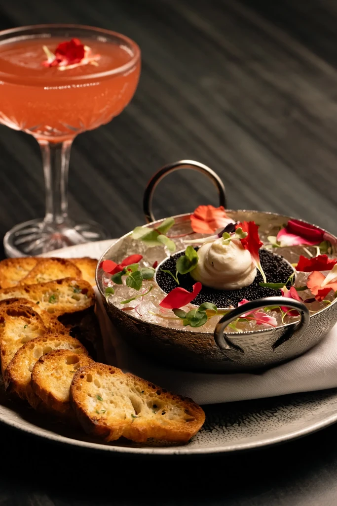 Caviar in hammered metal bowl on ice, crostini, and cocktail.
