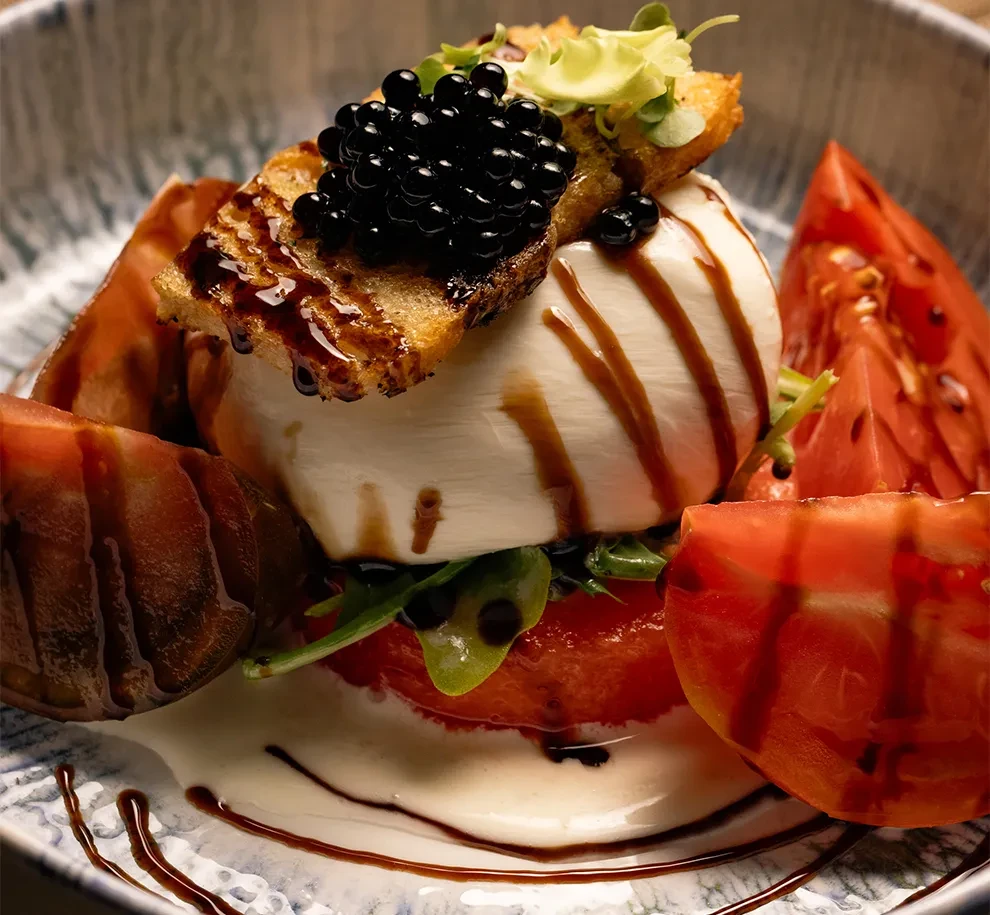 Burrata cheese with caviar, balsamic glaze, tomatoes, and green leaves.
