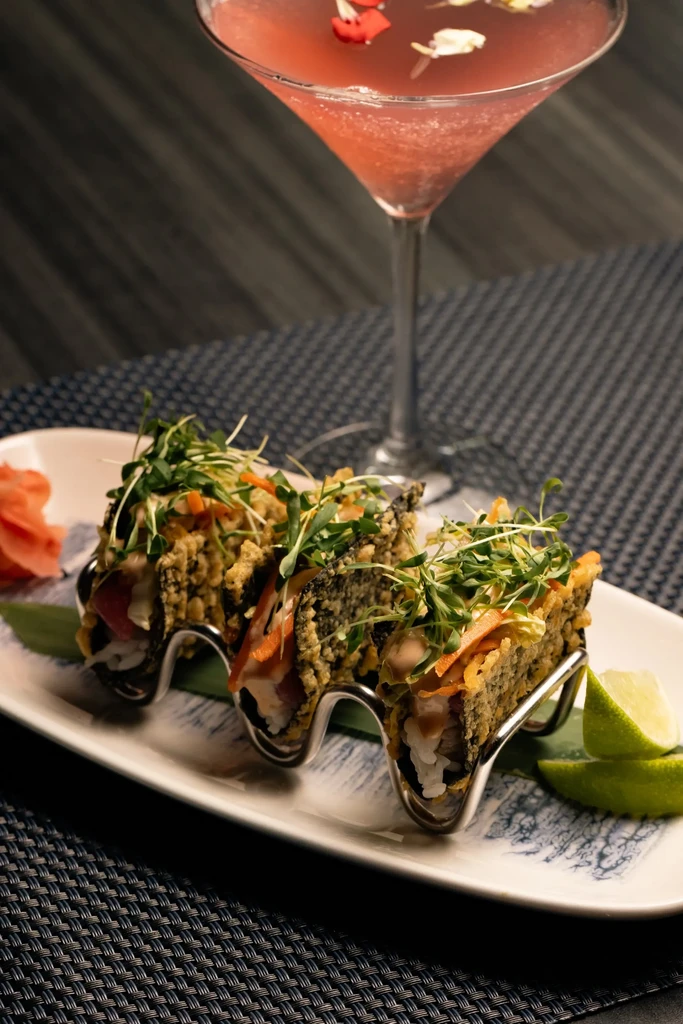 Three sushi tacos with raw fish, ginger, lime, and a cocktail.