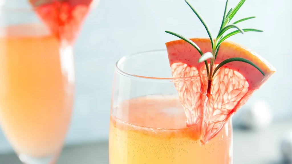 Two clear glasses with sparkling pink drinks, grapefruit, and rosemary.