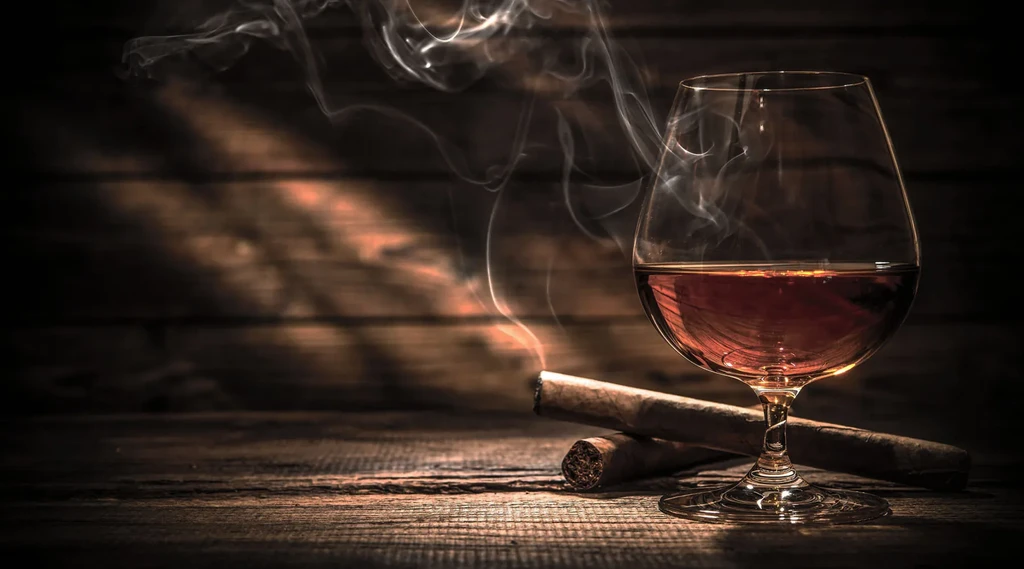 Amber spirit in glass, two cigars, one lit and smoking.