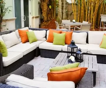 Outdoor patio with wicker sofa, colorful pillows, and wooden table.