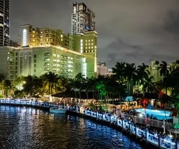 Illuminated green building by a busy night waterfront with reflecting lights.