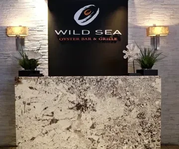 Restaurant reception desk, 'WILD SEA OYSTER BAR & GRILLE' sign, warm lighting.
